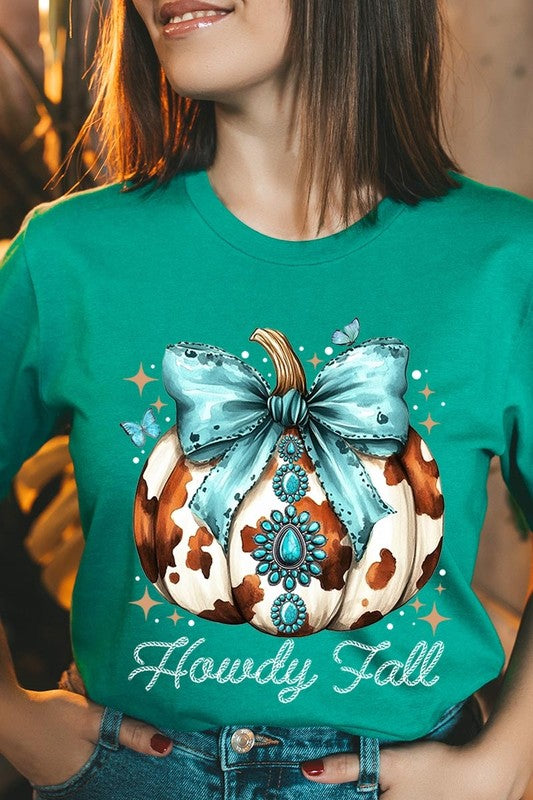 Person wearing the Howdy Fall Western Pumpkin Graphic Tee, featuring an illustrated pumpkin adorned with a blue bow and turquoise jewelry, along with the text "Howdy Fall." This beige unisex crew neck shirt pairs perfectly with their denim jacket.