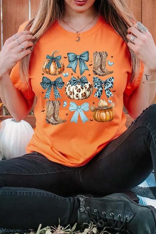 Person wearing a Turquoise Bow Western Fall Graphic Tee featuring illustrations of pumpkins, bows, cowboy hats, and boots adorned with blue and leopard print patterns. The high-quality printed design pairs perfectly with denim shorts and a denim jacket.