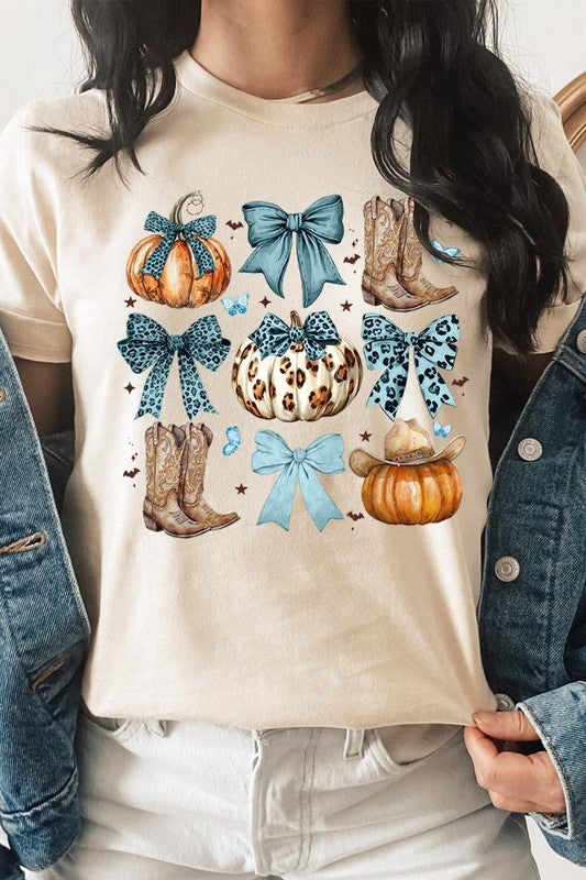 Person wearing a Turquoise Bow Western Fall Graphic Tee featuring illustrations of pumpkins, bows, cowboy hats, and boots adorned with blue and leopard print patterns. The high-quality printed design pairs perfectly with denim shorts and a denim jacket.