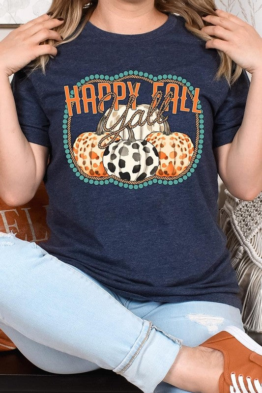 A person wearing a top-quality "Happy Fall Y'all" Graphic Tee featuring a design with three patterned pumpkins, paired with jeans and an orange cardigan, holds a pumpkin-shaped mug.