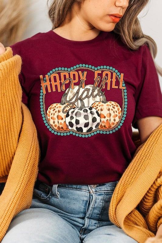 A person wearing a top-quality "Happy Fall Y'all" Graphic Tee featuring a design with three patterned pumpkins, paired with jeans and an orange cardigan, holds a pumpkin-shaped mug.