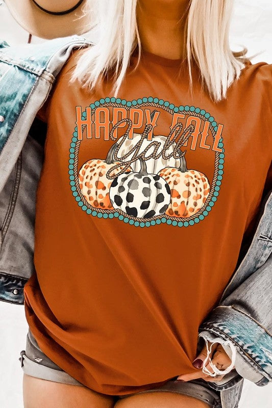 A person wearing a top-quality "Happy Fall Y'all" Graphic Tee featuring a design with three patterned pumpkins, paired with jeans and an orange cardigan, holds a pumpkin-shaped mug.