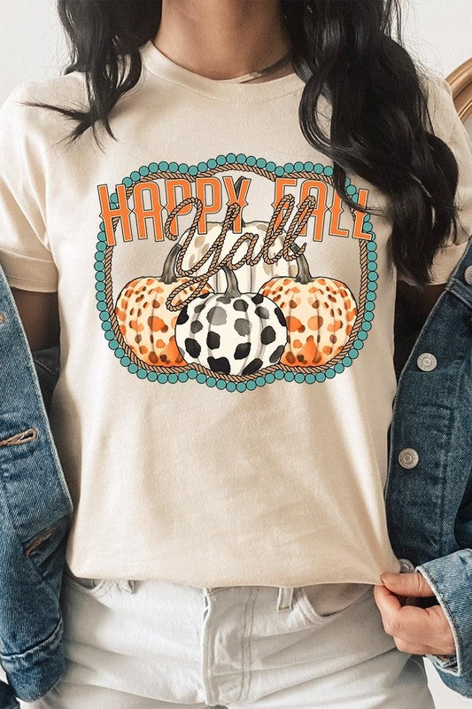 A person wearing a top-quality "Happy Fall Y'all" Graphic Tee featuring a design with three patterned pumpkins, paired with jeans and an orange cardigan, holds a pumpkin-shaped mug.