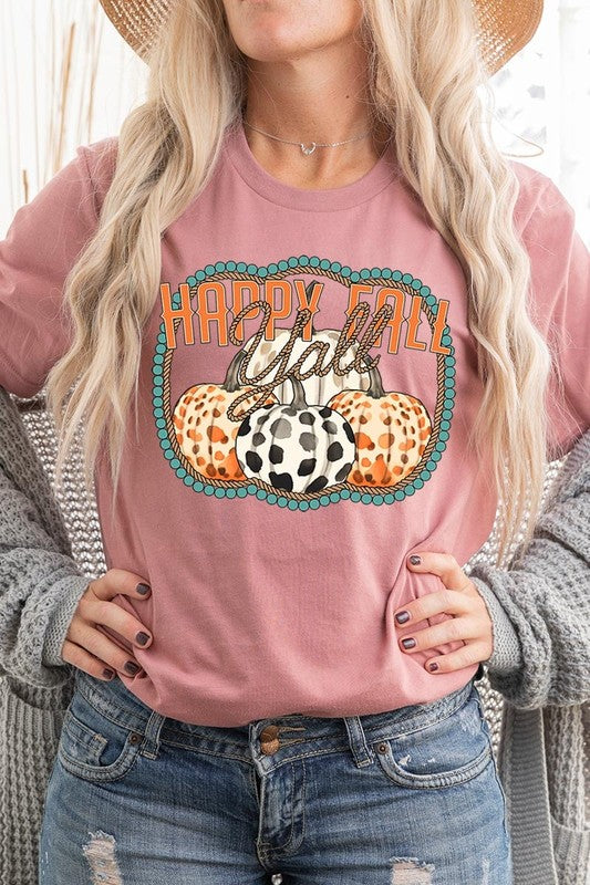 A person wearing a top-quality "Happy Fall Y'all" Graphic Tee featuring a design with three patterned pumpkins, paired with jeans and an orange cardigan, holds a pumpkin-shaped mug.