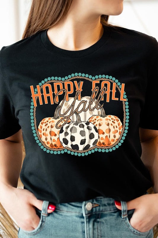 A person wearing a top-quality "Happy Fall Y'all" Graphic Tee featuring a design with three patterned pumpkins, paired with jeans and an orange cardigan, holds a pumpkin-shaped mug.