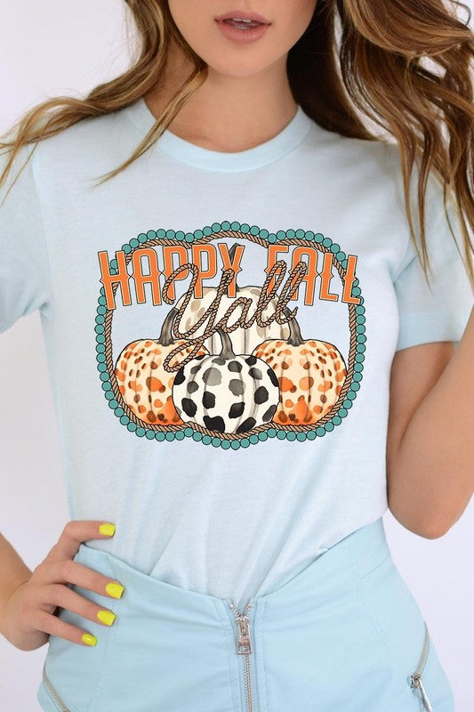 A person wearing a top-quality "Happy Fall Y'all" Graphic Tee featuring a design with three patterned pumpkins, paired with jeans and an orange cardigan, holds a pumpkin-shaped mug.