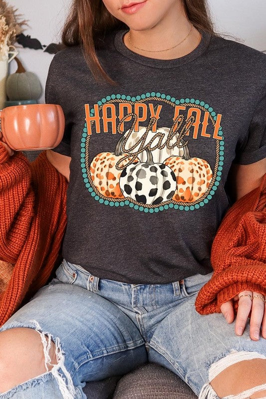 A person wearing a top-quality "Happy Fall Y'all" Graphic Tee featuring a design with three patterned pumpkins, paired with jeans and an orange cardigan, holds a pumpkin-shaped mug.