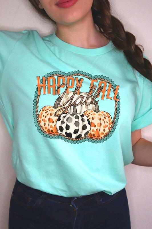 A person wearing a top-quality "Happy Fall Y'all" Graphic Tee featuring a design with three patterned pumpkins, paired with jeans and an orange cardigan, holds a pumpkin-shaped mug.