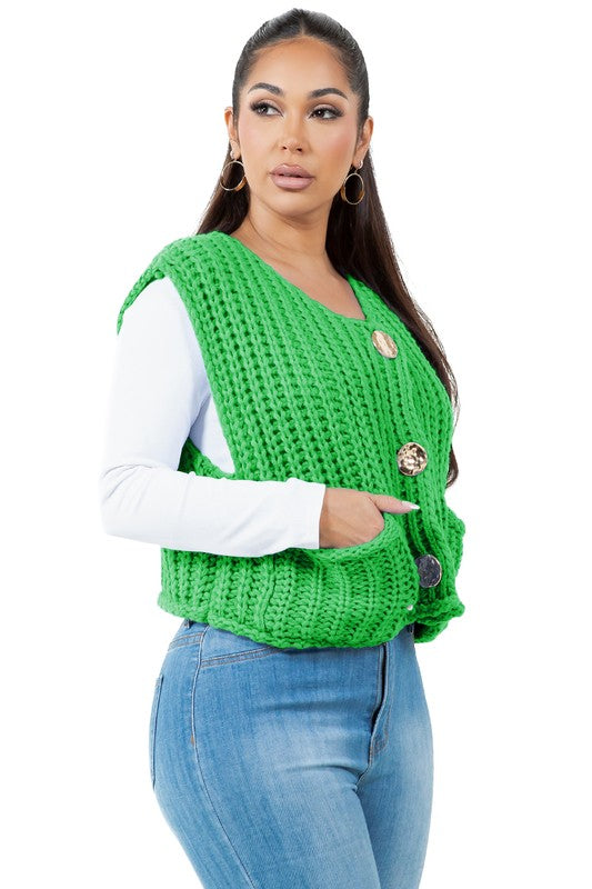 A woman with long dark hair wearing a green WOMEN FASHION KNITWEAR VEST with large buttons over a white long-sleeve shirt and blue jeans.