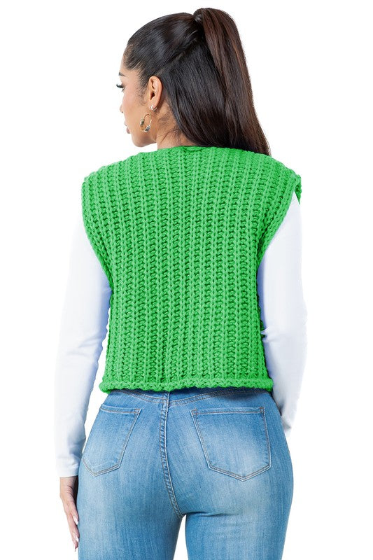 A woman with long dark hair wearing a green WOMEN FASHION KNITWEAR VEST with large buttons over a white long-sleeve shirt and blue jeans.