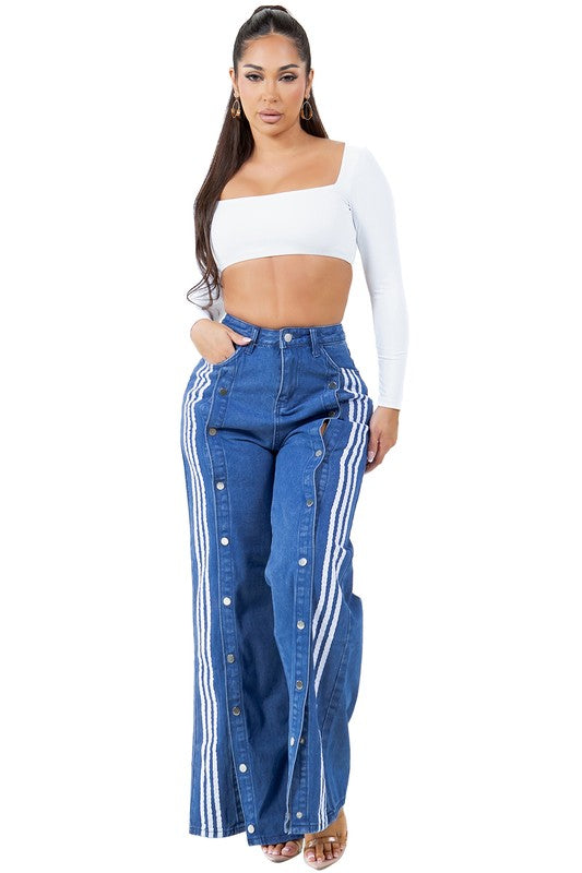 A woman with long dark hair wears a white cropped top paired with WOMEN FASHION CASUAL STYLE DENIM PANTS, which feature high-waist, wide-leg design with blue fabric adorned by white stripes and button details down the sides.