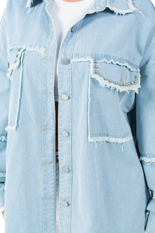 A woman is standing, wearing the WOMEN FASHION OVERSIZE DENIM SHIRT with long sleeves over a white top and white pants, paired with beige high-heeled sandals.