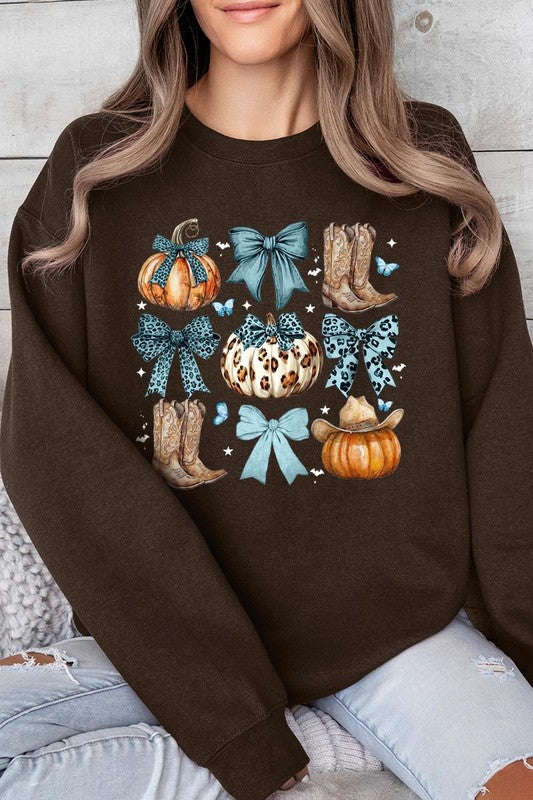 A woman is wearing a high-quality Turquoise Bow Western Fall Fleece Sweatshirt in olive green, featuring pumpkins, cowboy boots, a hat, and turquoise bows. She is seated on a gray, textured surface and wears light blue ripped jeans.