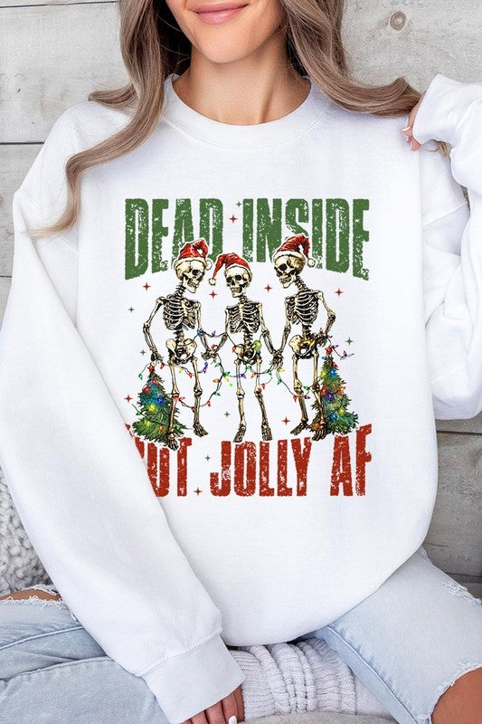 A person is wearing a "Dead Inside But Jolly AF Skeleton Sweatshirt," a beige unisex crew neck sweatshirt featuring a festive design of three dancing skeletons in Santa hats. The high-quality direct to film printed graphic text reads, "DEAD INSIDE BUT JOLLY AF.