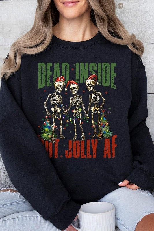 A person is wearing a "Dead Inside But Jolly AF Skeleton Sweatshirt," a beige unisex crew neck sweatshirt featuring a festive design of three dancing skeletons in Santa hats. The high-quality direct to film printed graphic text reads, "DEAD INSIDE BUT JOLLY AF.