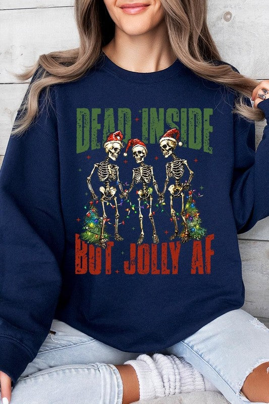 A person is wearing a "Dead Inside But Jolly AF Skeleton Sweatshirt," a beige unisex crew neck sweatshirt featuring a festive design of three dancing skeletons in Santa hats. The high-quality direct to film printed graphic text reads, "DEAD INSIDE BUT JOLLY AF.