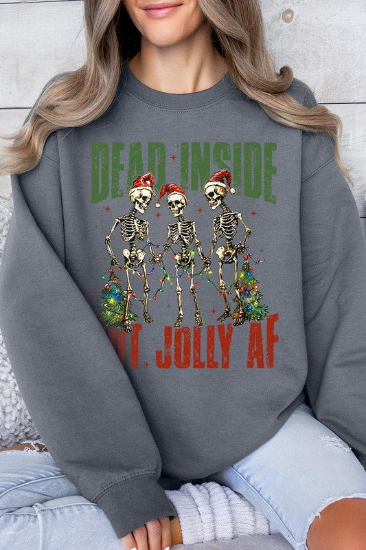 A person is wearing a "Dead Inside But Jolly AF Skeleton Sweatshirt," a beige unisex crew neck sweatshirt featuring a festive design of three dancing skeletons in Santa hats. The high-quality direct to film printed graphic text reads, "DEAD INSIDE BUT JOLLY AF.