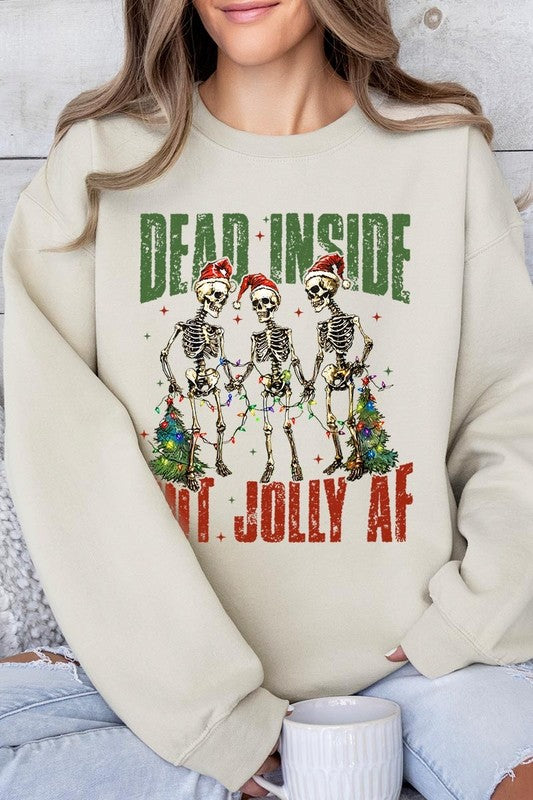 A person is wearing a "Dead Inside But Jolly AF Skeleton Sweatshirt," a beige unisex crew neck sweatshirt featuring a festive design of three dancing skeletons in Santa hats. The high-quality direct to film printed graphic text reads, "DEAD INSIDE BUT JOLLY AF.