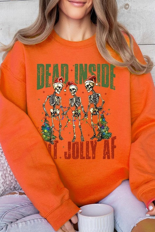 A person is wearing a "Dead Inside But Jolly AF Skeleton Sweatshirt," a beige unisex crew neck sweatshirt featuring a festive design of three dancing skeletons in Santa hats. The high-quality direct to film printed graphic text reads, "DEAD INSIDE BUT JOLLY AF.