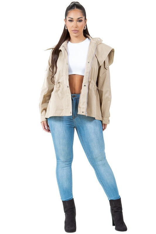 A person stands wearing a tan, water-repellent WOMEN FASHION TRENCH COAT over a white top, paired with blue jeans.