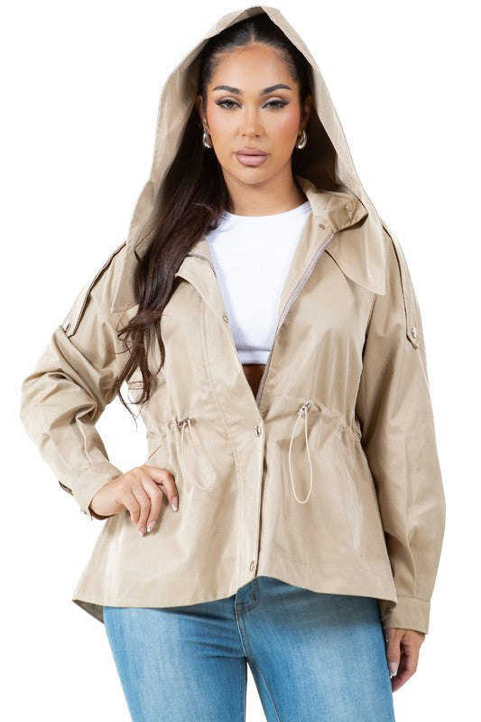 A person stands wearing a tan, water-repellent WOMEN FASHION TRENCH COAT over a white top, paired with blue jeans.