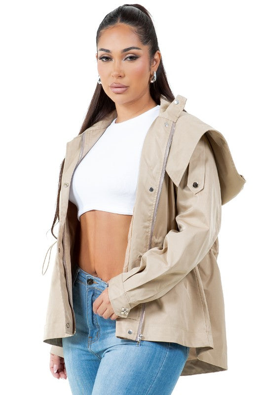 A person stands wearing a tan, water-repellent WOMEN FASHION TRENCH COAT over a white top, paired with blue jeans.