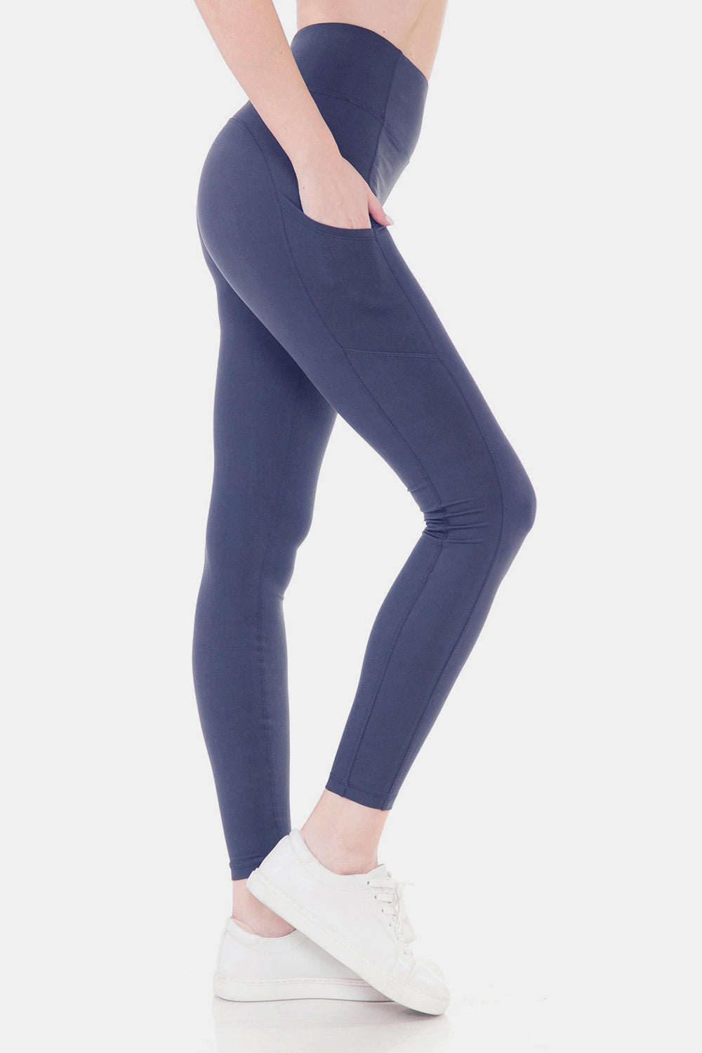 A person is shown from the side wearing Leggings Depot High Waist Wide Waistband Leggings in navy blue, which feature convenient pockets and are paired with white sneakers. The stretchy fabric of the leggings adds comfort and flexibility to their active look.