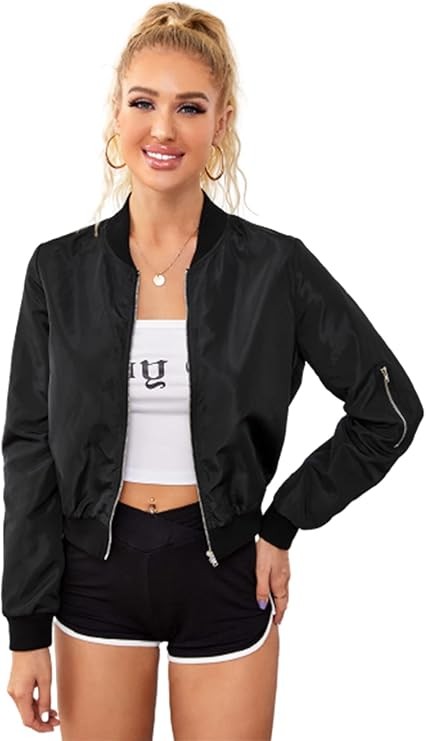 A person with a ponytail is wearing the Women Bomber Jacket in a sleek black design, expertly zipping it up over a white crop top, and pairing it with black polyester shorts trimmed in white.