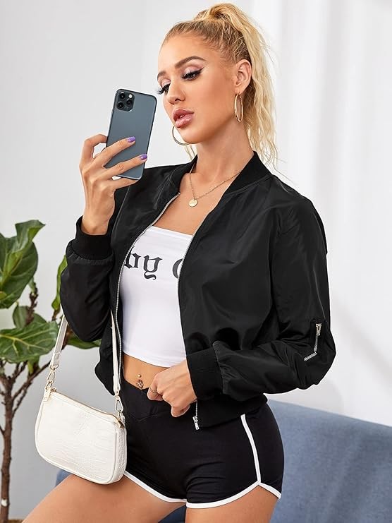 A person with a ponytail is wearing the Women Bomber Jacket in a sleek black design, expertly zipping it up over a white crop top, and pairing it with black polyester shorts trimmed in white.