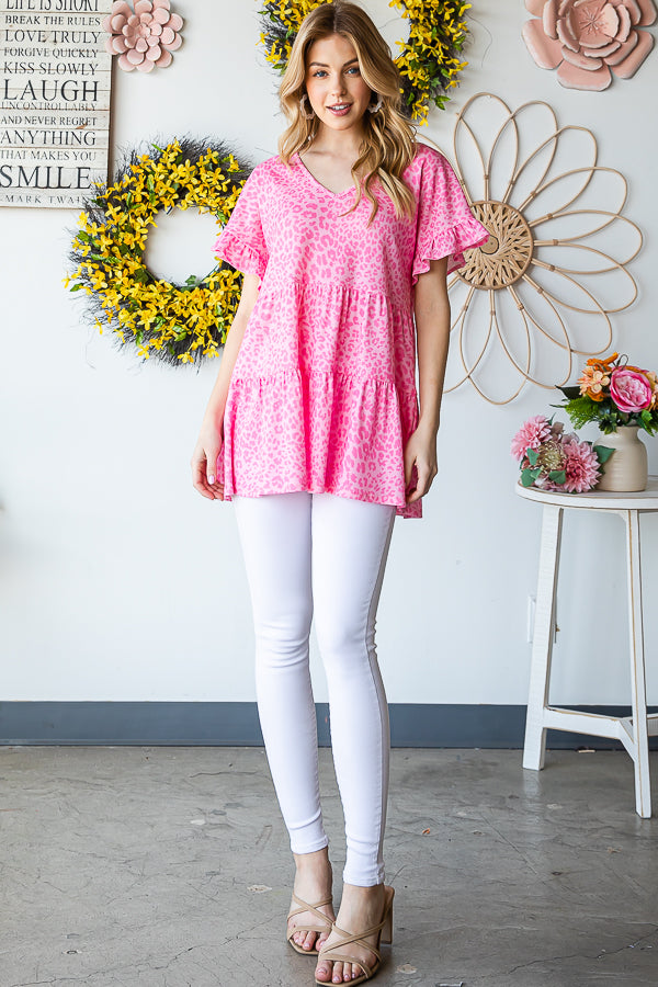 A person wearing a Heimish Full Size Leopard Ruffle Trim Short Sleeve Top stands in front of a floral wreath display.