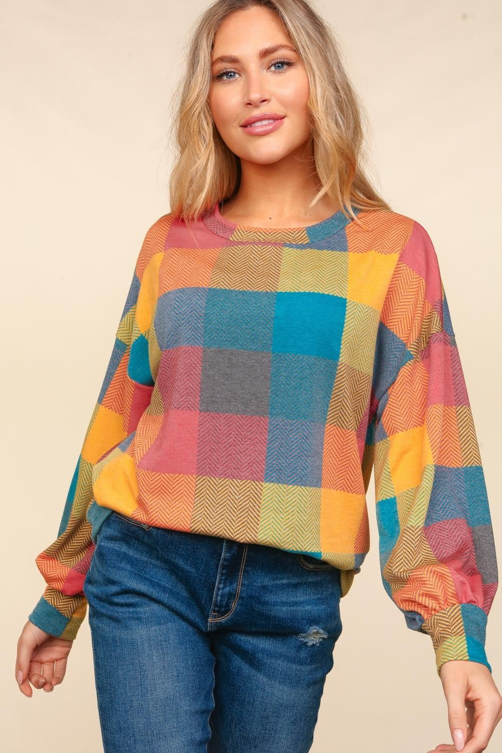 A woman wearing a stylish Haptics Round Neck Color Block Plaid Top and blue jeans poses against a beige background.