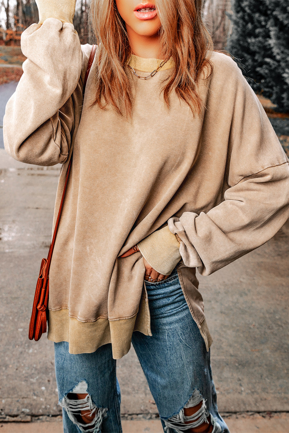 Person with wavy blonde hair wearing a Khaki Drop Shoulder Ribbed Trim Oversized Sweatshirt and blue jeans, walking outdoors with a brown leather crossbody bag.