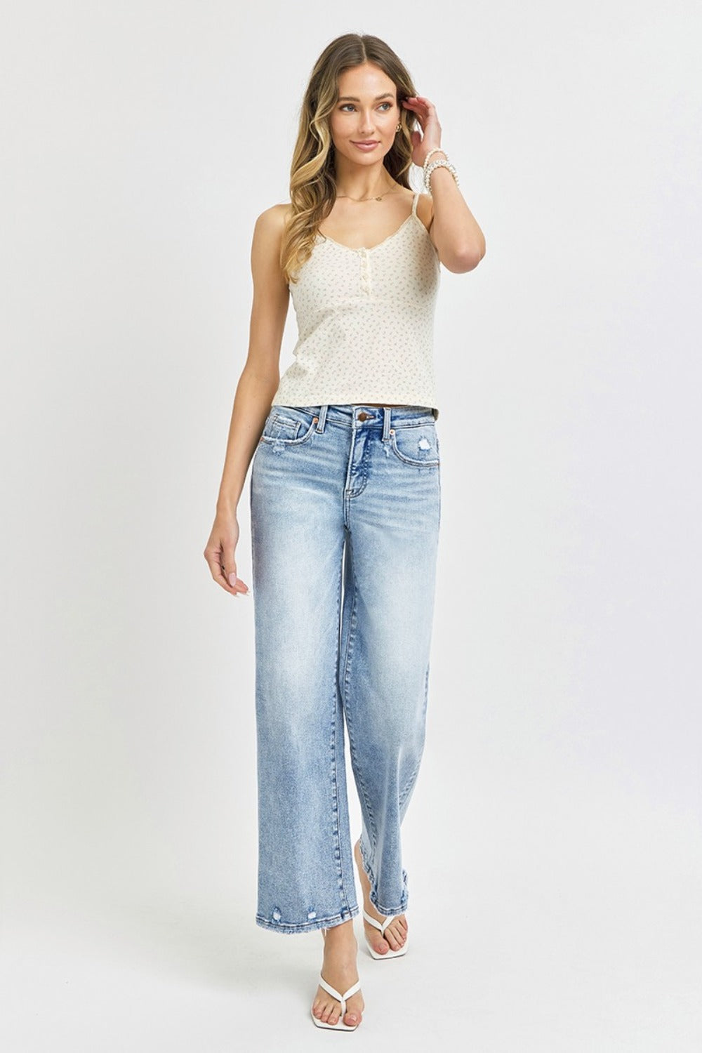 A person wearing RISEN Full Size Tummy Control High Rise Crop Wide Leg Jeans in a light-wash with a frayed hem and white open-toe sandals.