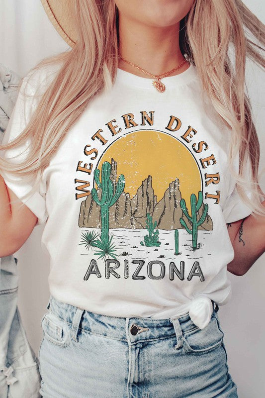 A person wearing the WESTERN DESERT ARIZONA Graphic Tee showcases a bold design featuring cacti and a mountainous landscape against a setting sun. With unisex sizing, this tee is perfect for anyone who loves desert vibes.