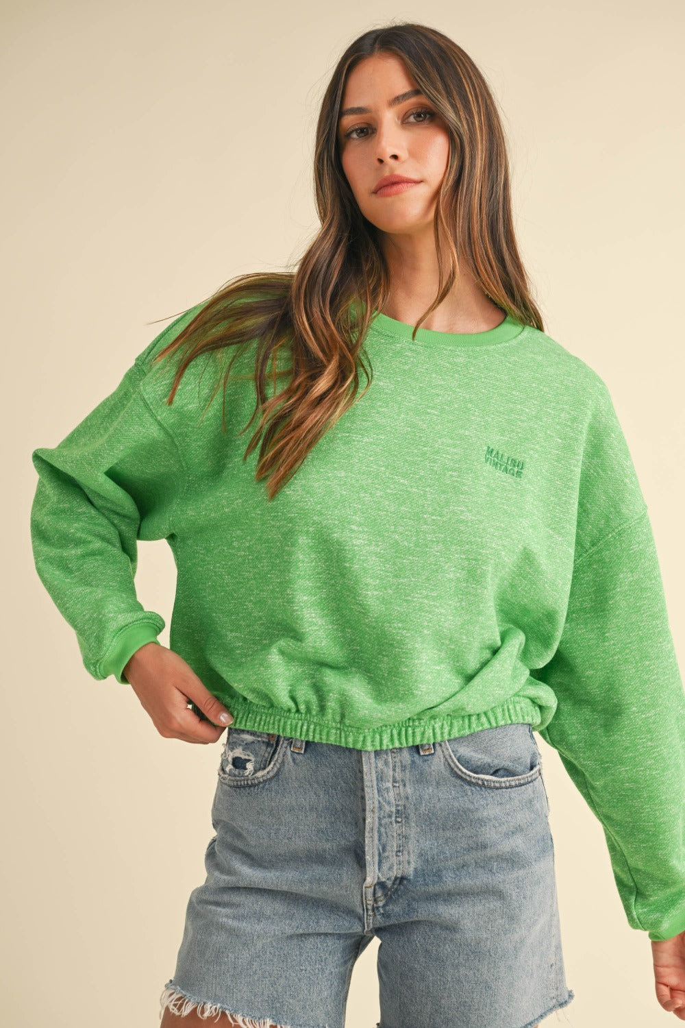 A woman models a Mable Round Neck Letter Embroidery Crop Sweatshirt in green, paired with denim shorts, against a plain background, effortlessly showcasing her street style.