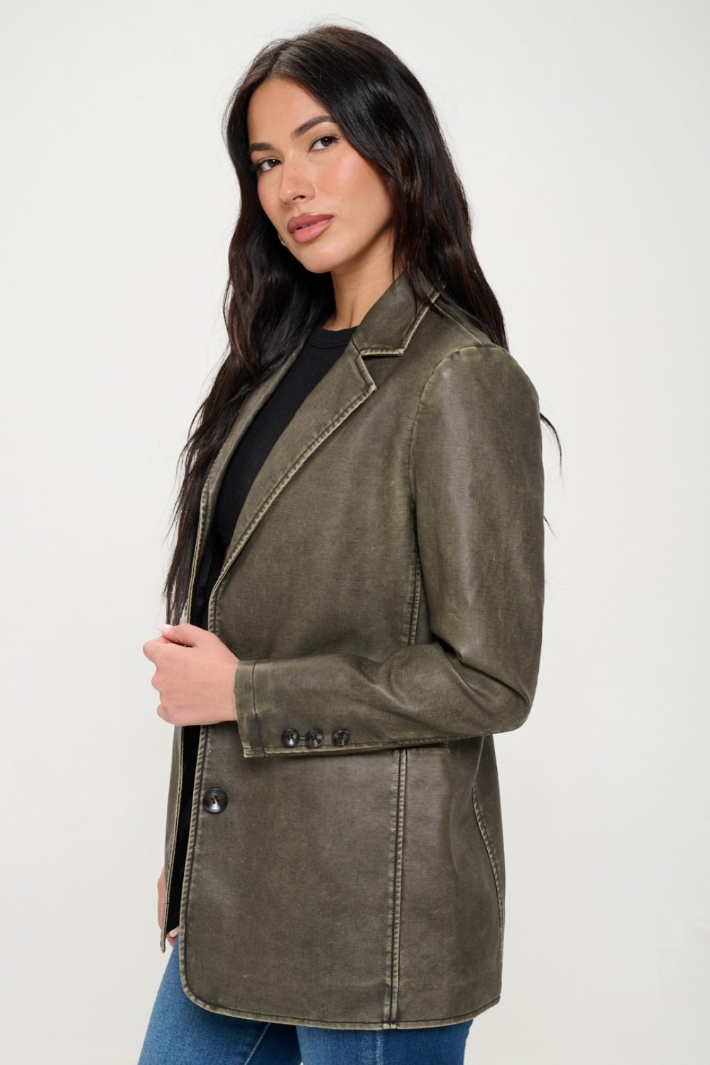 A person with long dark hair wears the Coalition LA Single-Breasted Vegan Leather Blazer in olive green over a black crop top and blue jeans against a neutral background, showcasing a stylish and ethical fashion choice.