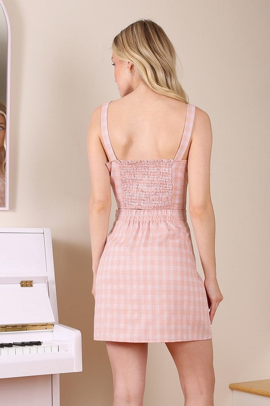 A woman dressed in an SL pattern crop top & skirt set is seated on wooden stairs, gazing downward.