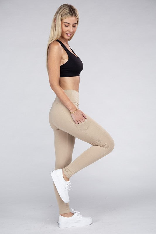 A person is wearing high-waisted dark gray Active Leggings Featuring Concealed Pockets, a bracelet on their left wrist, and white sneakers. The background is a plain light gray.