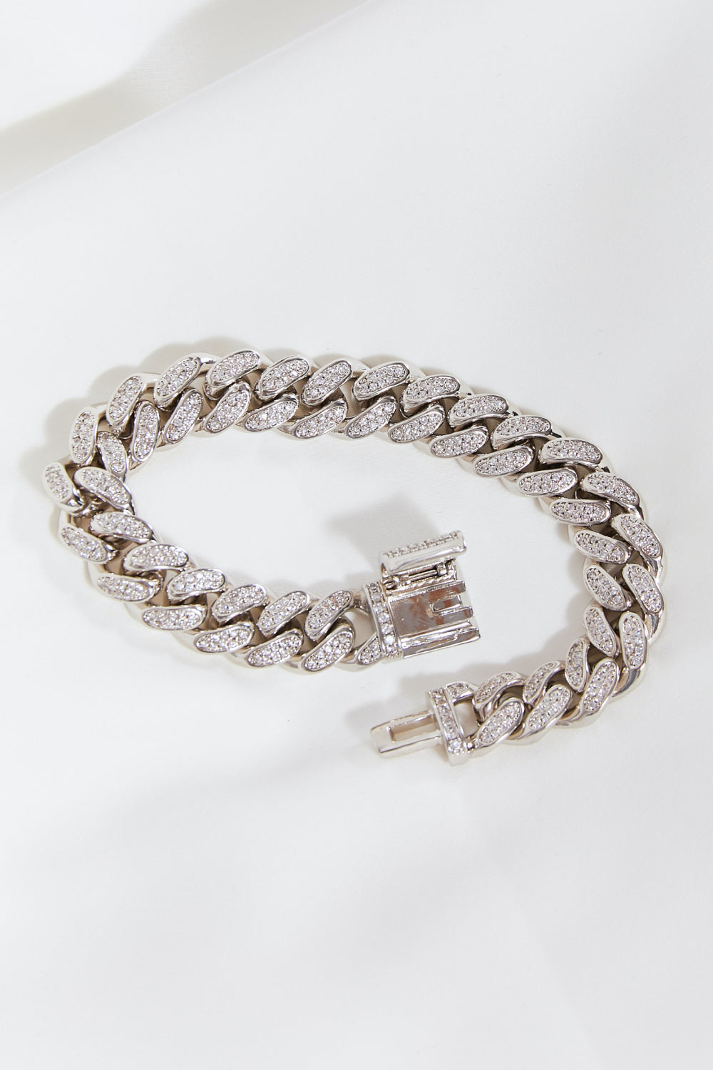 The Curb Chain Bracelet, crafted from silver and adorned with sparkling diamonds, elegantly graces the wrist against a white background.