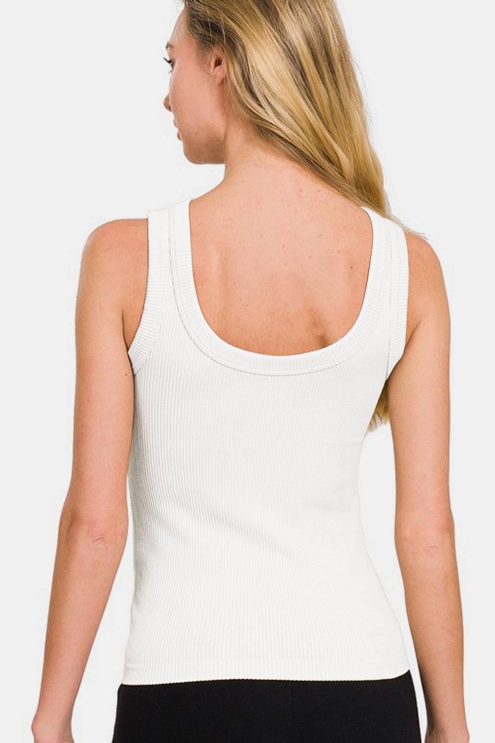 A woman with long blonde hair wears the Zenana 2 Way Neckline Washed Ribbed Tank in white, paired with black pants. She stands against a plain white background, highlighting her versatile wardrobe choices.