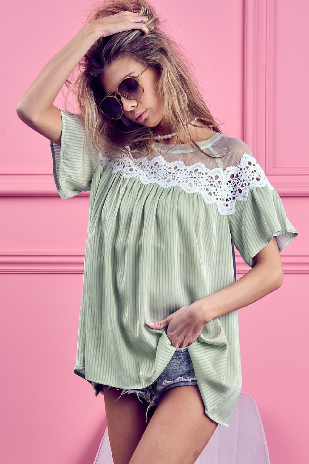 A woman wearing a BiBi Lace Detail Short Sleeve Striped Blouse and sunglasses poses against a pink background.