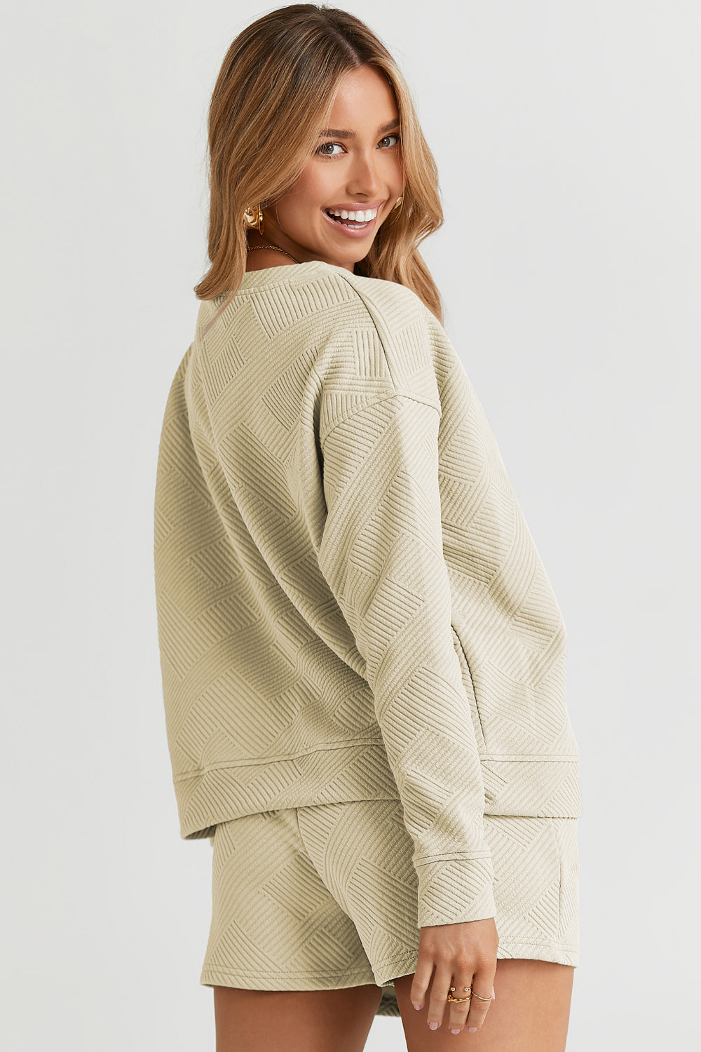 A woman decked out in the Double Take Full Size Texture Long Sleeve Top and Drawstring Shorts Set, featuring a brown textured two-piece with a long-sleeve top and matching pocketed shorts, smiles at the camera.