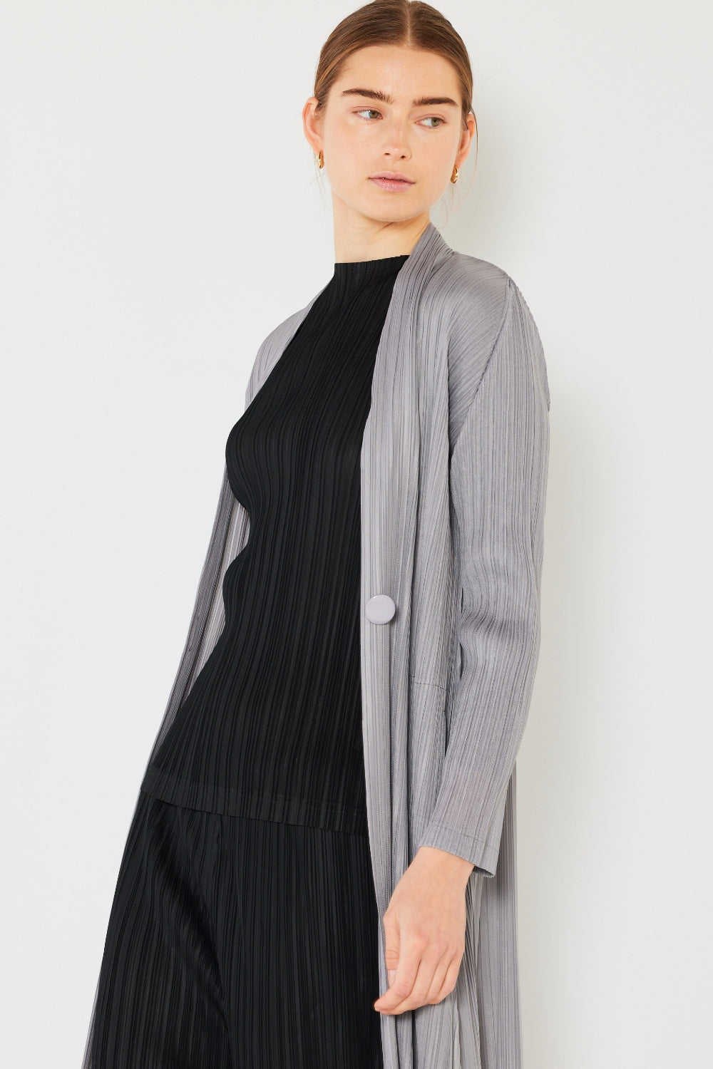 A person wears the Marina West Swim Pleated Long Sleeve Cardigan over a matching top and gray wide-leg pants, standing against a plain light background. This versatile layering piece, with its chic pleated long sleeves, adds an elegant touch to the ensemble.