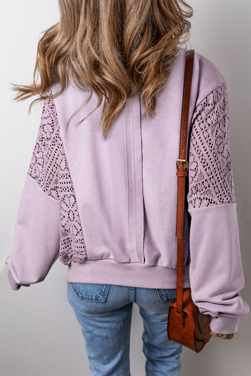 A person with long hair is seen from the back wearing the Orchid Petal Knit Crochet Exposed Seam Ribbed Trim Sweatshirt, blue jeans, and a brown crossbody bag.