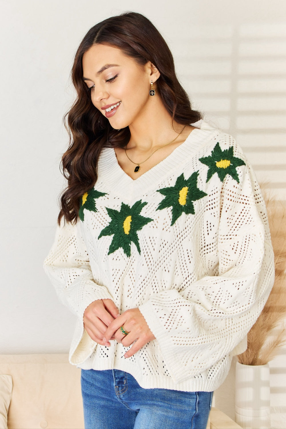 A woman wearing the POL Floral Embroidered Pattern V-Neck Sweater in creamy chenille paired with blue jeans, standing indoors.