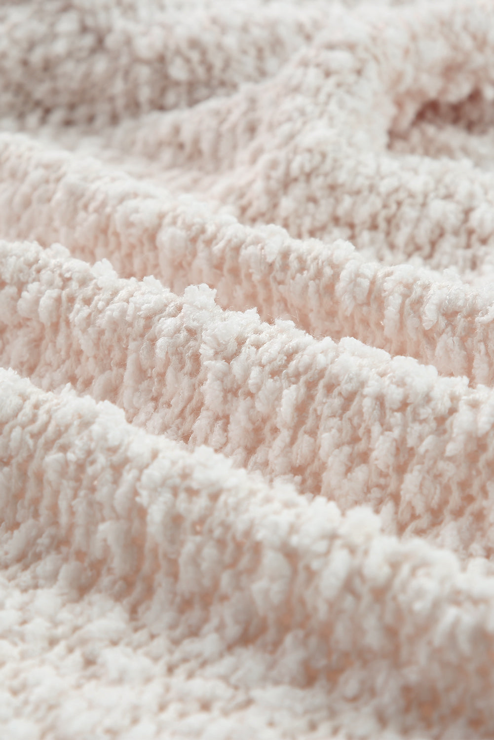 A woman in an Apricot Popcorn Knit Open Front Cardigan and jeans stands against a brick wall, looking to the side with a slight smile.