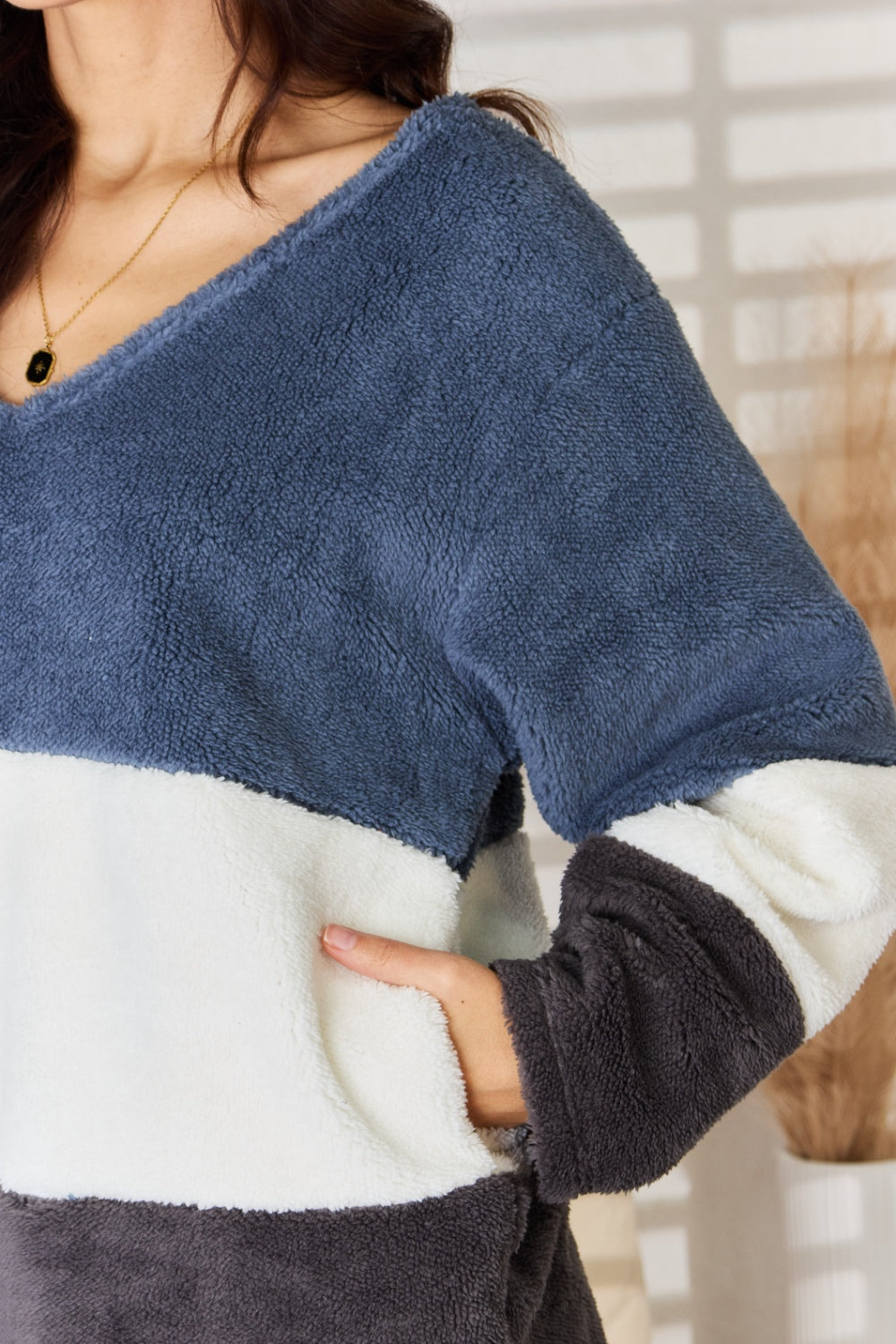 A woman with long, dark hair smiles while wearing the Culture Code Faux Fur Color Block V-Neck Sweater in shades of navy, white, and gray, paired with blue jeans—a versatile wardrobe addition.