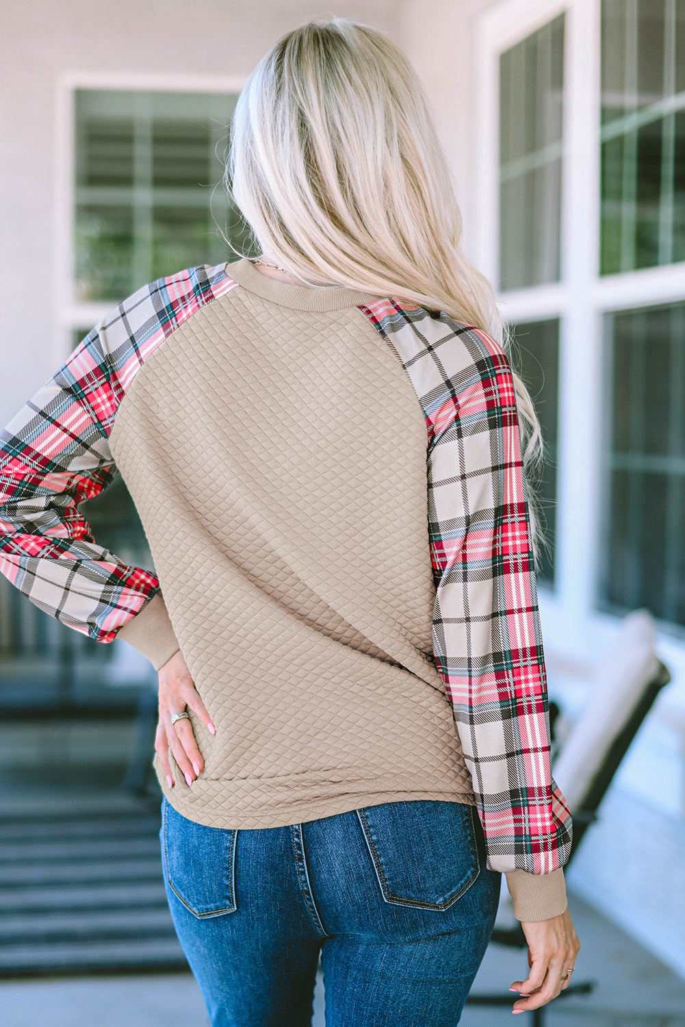 A person with long blonde hair stands with their back to the camera, wearing an Apricot Plaid Raglan Sleeve Sweatshirt and blue jeans.