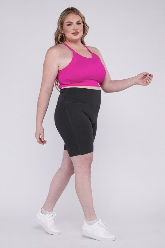 Against a plain background, a person showcases the Plus Athletic High Rise Biker Shorts in coral, crafted from high-quality athletic fabric and paired with a pink top.