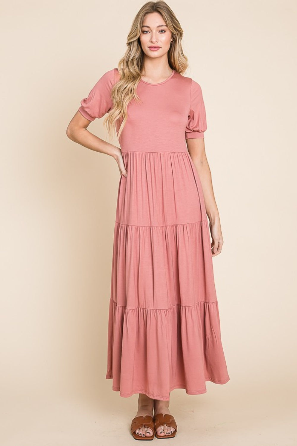 A person wearing the BOMBOM Short Sleeve Tiered Maxi Dress in pink, showcasing its comfortable style with a long, tiered design, stands against a beige background.